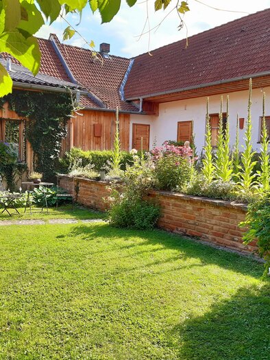 Ein schöner Garten mit grünem Rasen und bunten Blumen. Im Hintergrund sind Häuser mit roten Dächern zu sehen. | © Familie Brugner
