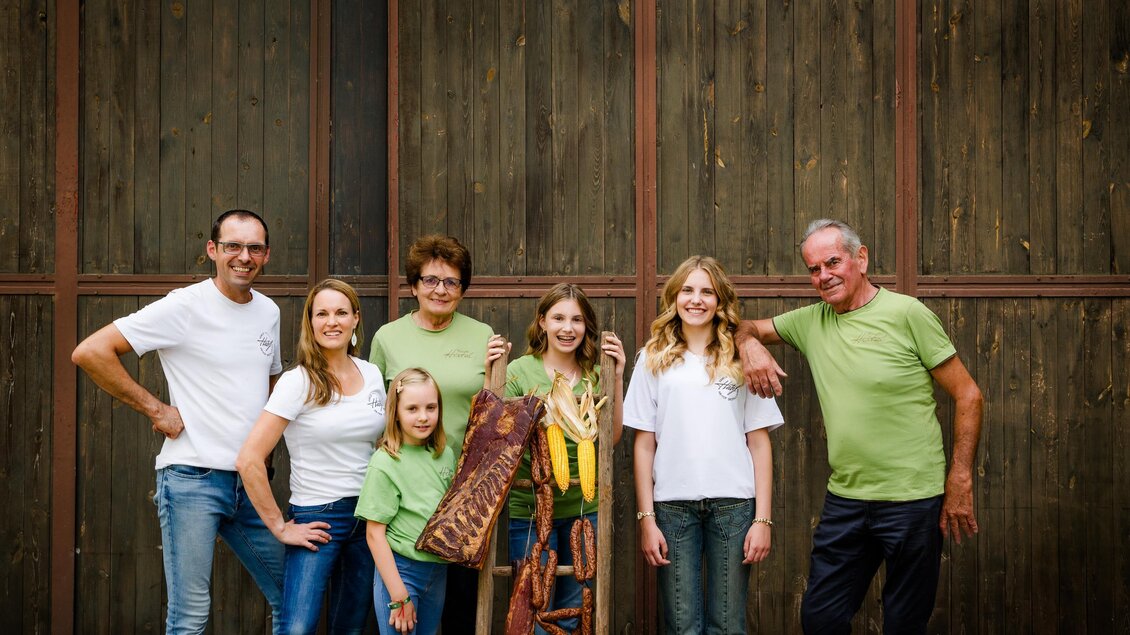 Eine Gruppe von sieben Personen steht vor einer Holzwand. Sie lächeln und tragen verschiedene T-Shirts in hellen Farben. | © Region Graz - Mias Photoart