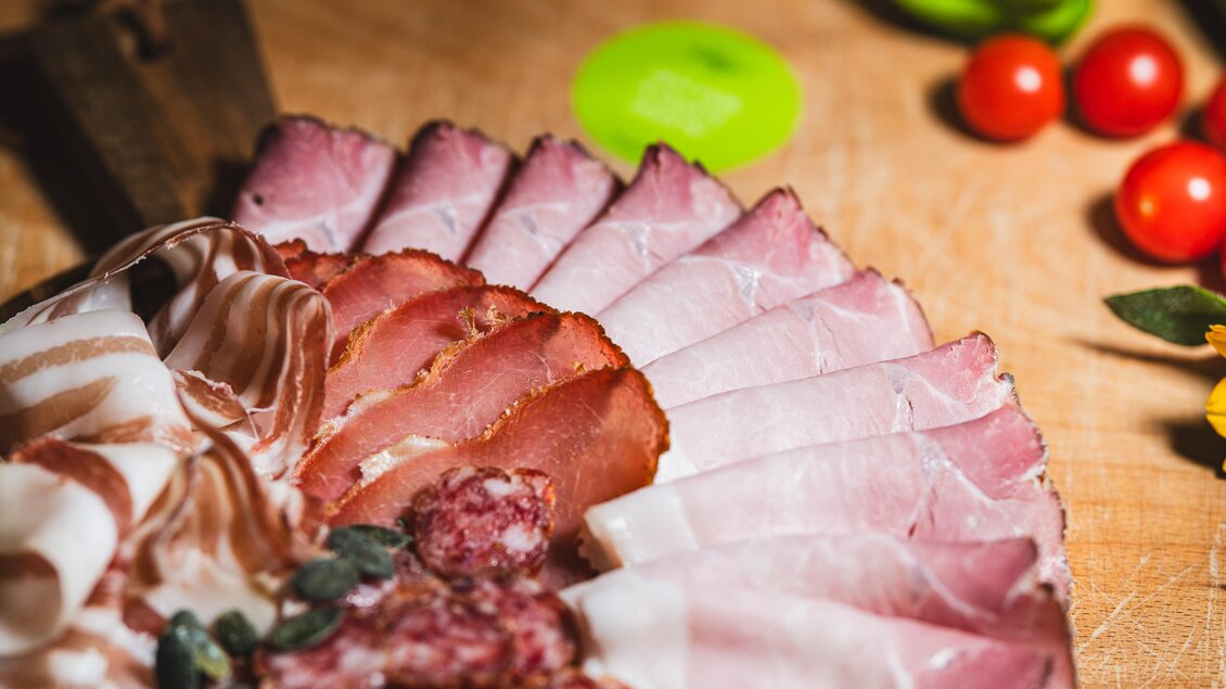 Eine appetitliche Auswahl an Wurst und Schinken auf einem Holzbrett. Frische Kräuter und Cherrytomaten ergänzen die Präsentation. | © Region Graz - Mias Photoart