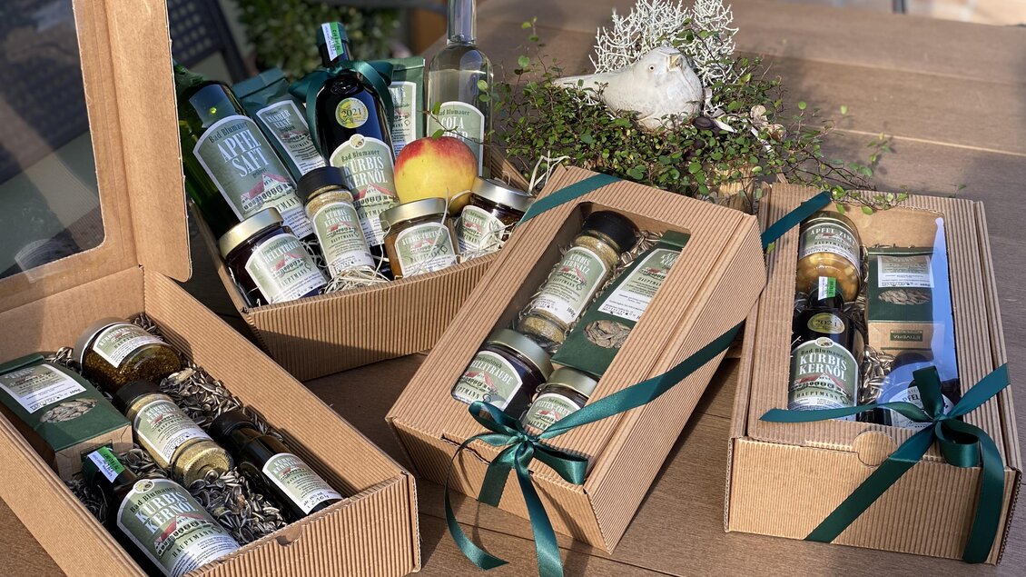 Körbe mit verschiedenen Produkten in stilvollen Verpackungen. Die Präsentation enthält Gläser, Flaschen und einen Apfel, dekoriert mit grünen Schleifen. | © Hofladen Hauptmann
