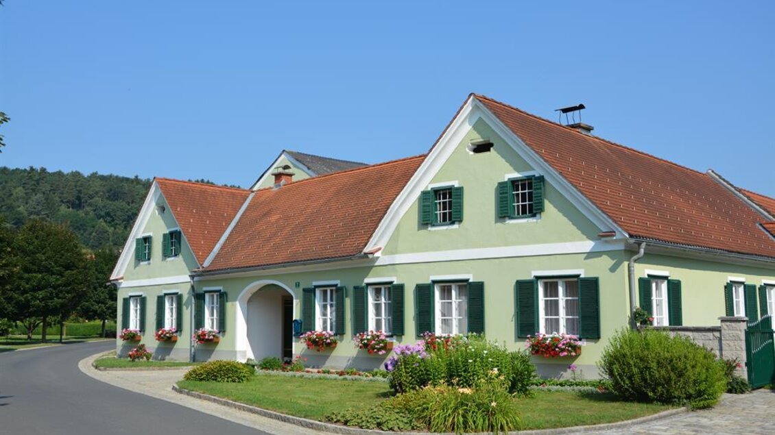 Ein hübsches Haus mit grünem Anstrich und rotem Dach. Es steht in einer ruhigen Umgebung mit Bäumen und Blumen. | © Hofladen Hauptmann