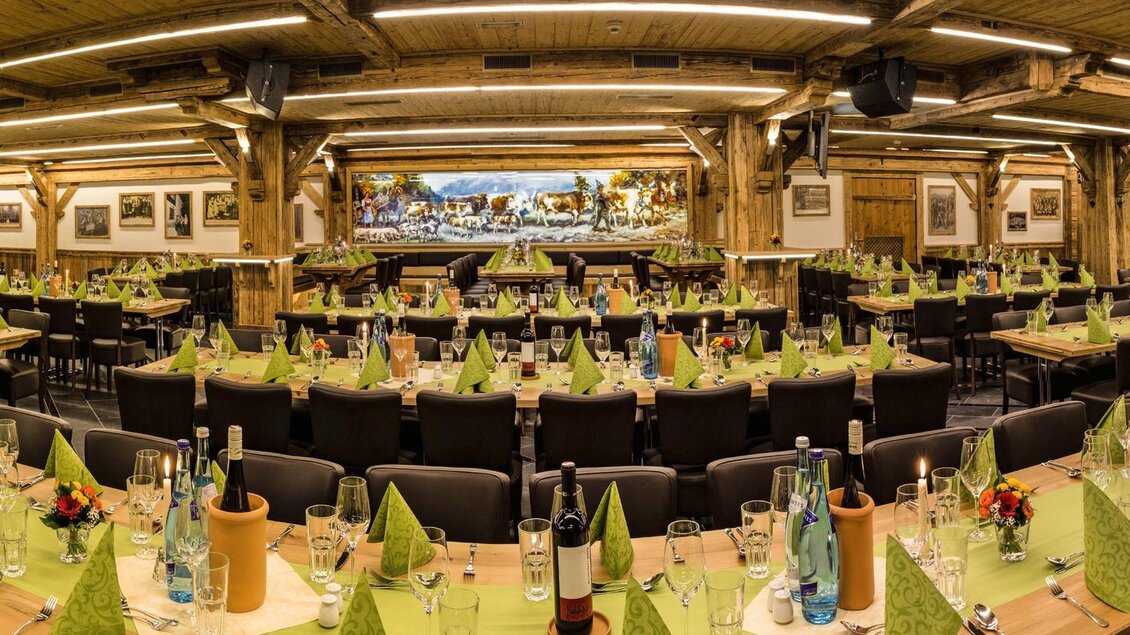 Ein gemütlicher Innenraum mit langen Tischen und Stühlen, die für eine Veranstaltung vorbereitet sind. Grüne Servietten und Flaschen stehen auf jedem Tisch, um eine festliche Atmosphäre zu schaffen. | © AIR-Media.at