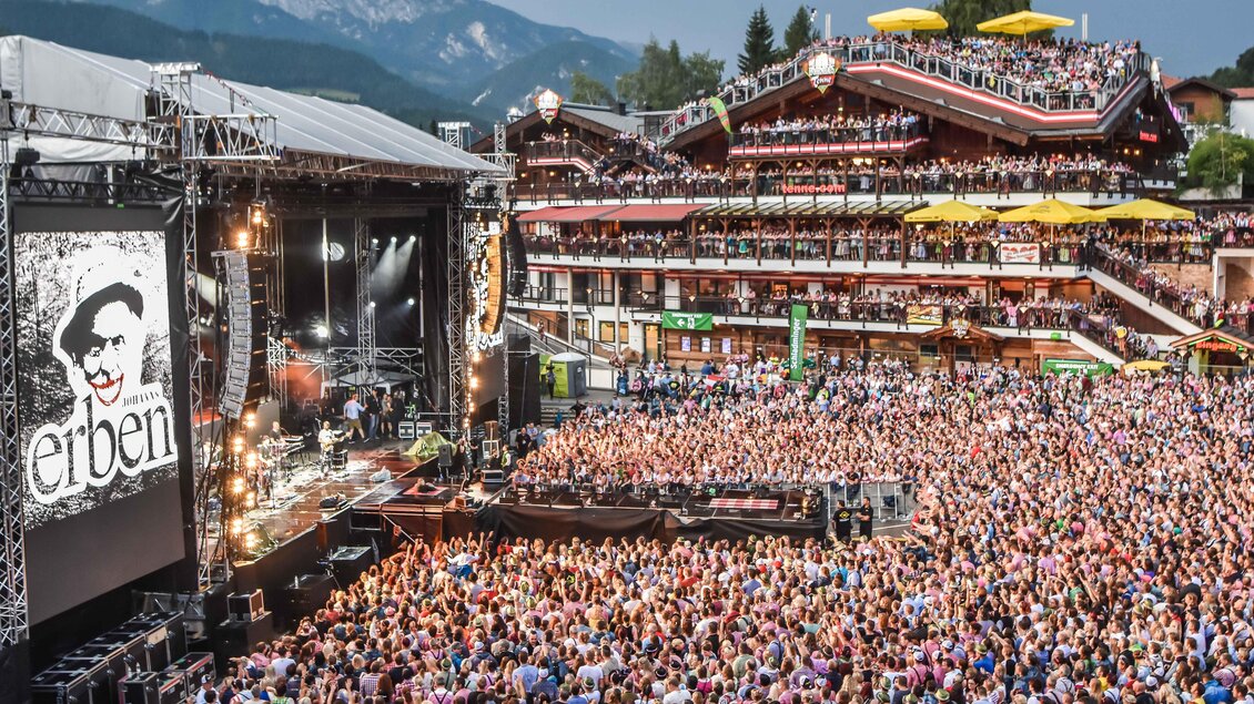 Ein großes Open-Air-Konzert mit einer riesigen Menschenmenge. Im Hintergrund sind die Berge und die festlich dekorierten Gebäude zu sehen. | © Pressefoto Scharinger