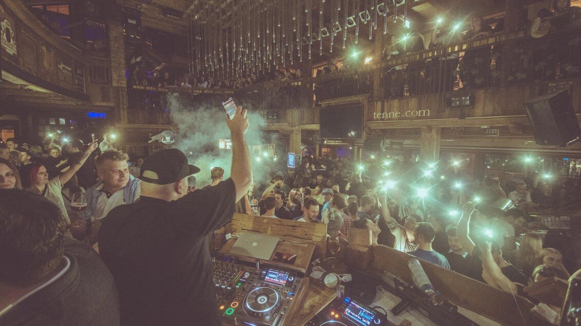 Ein DJ steht vor einer belebten Tanzfläche und hebt die Hand, während das Publikum mit Licht quellen begeistert ist. Die Atmosphäre ist lebhaft und festlich, mit einer großen Menschenmenge. | © Pressefoto Scharinger