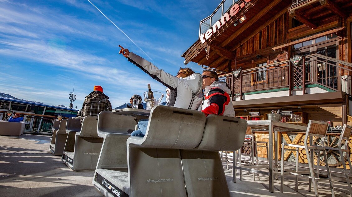 Eine Gruppe von Personen sitzt auf modernen Sitzmöbeln und blickt nach draußen. Im Hintergrund ist ein Holzgebäude mit einer Terrasse zu sehen. | © AIR-Media.at