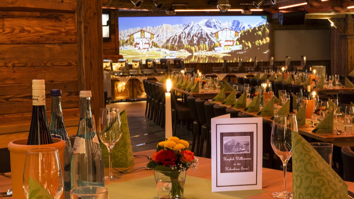 Ein einladendes Restaurant mit einem holzverkleideten Interieur. Der Tisch ist festlich gedeckt, mit Kerzenlicht und Blumenarrangement. | © AIR-Media.at