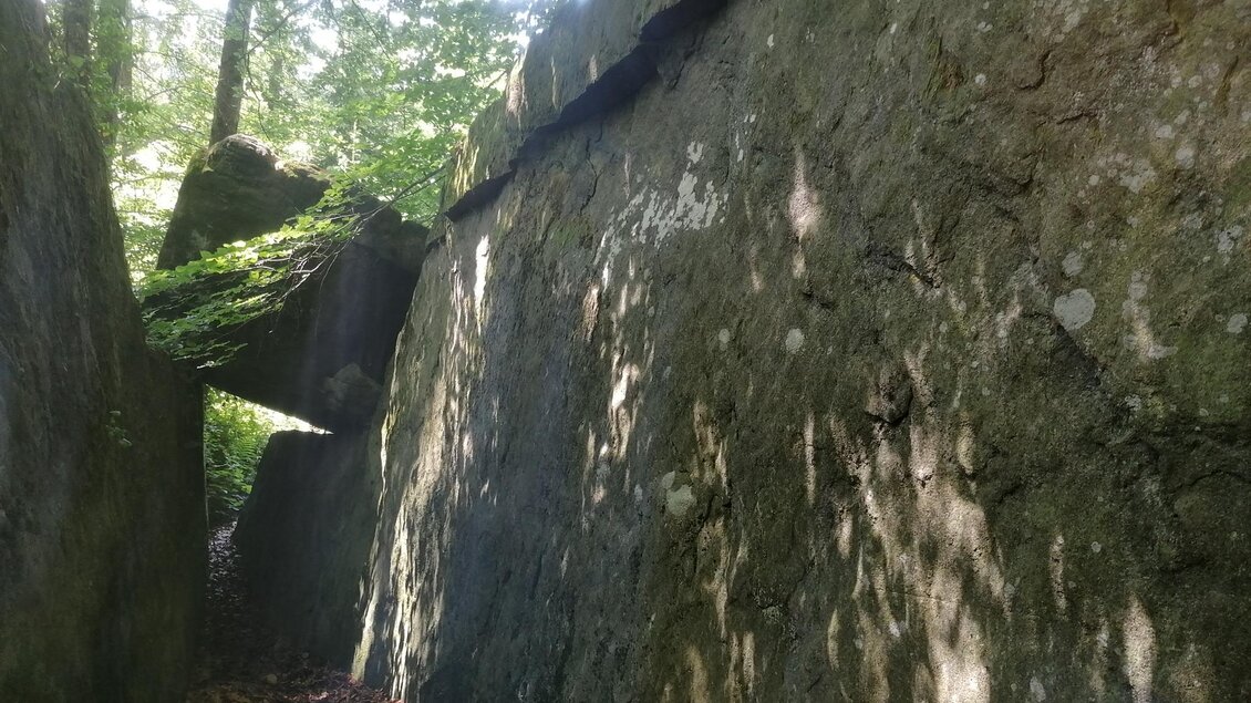 Ein schmaler Pfad zwischen großen, moosbewachsenen Felsblöcken im Wald. Das Licht fällt durch die Bäume und erzeugt interessante Schattenmuster auf den Steinen. | © Hohlkogel - Hohlfelsen