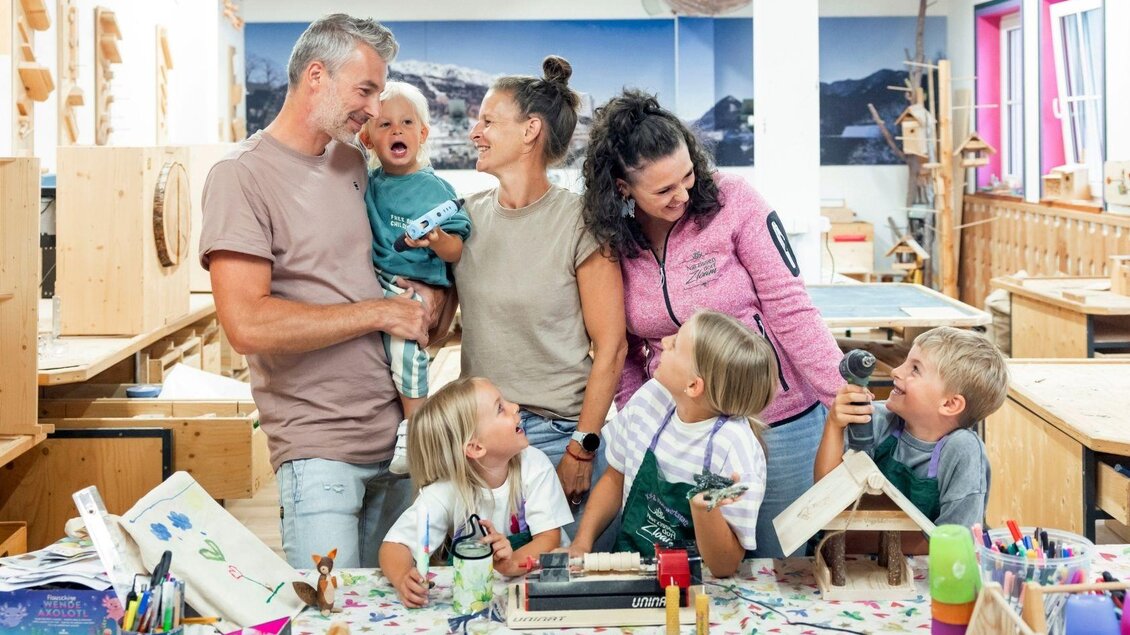 Eine fröhliche Gruppe von Erwachsenen und Kindern in einem kreativen Workshop. Sie arbeiten an verschiedenen Bastelprojekten an einem bunten Tisch. | © www.zloam.at