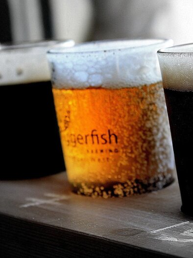 A row of beer glasses on a wooden board. The middle glass contains a golden beer, while the others are darker. | © pixabay