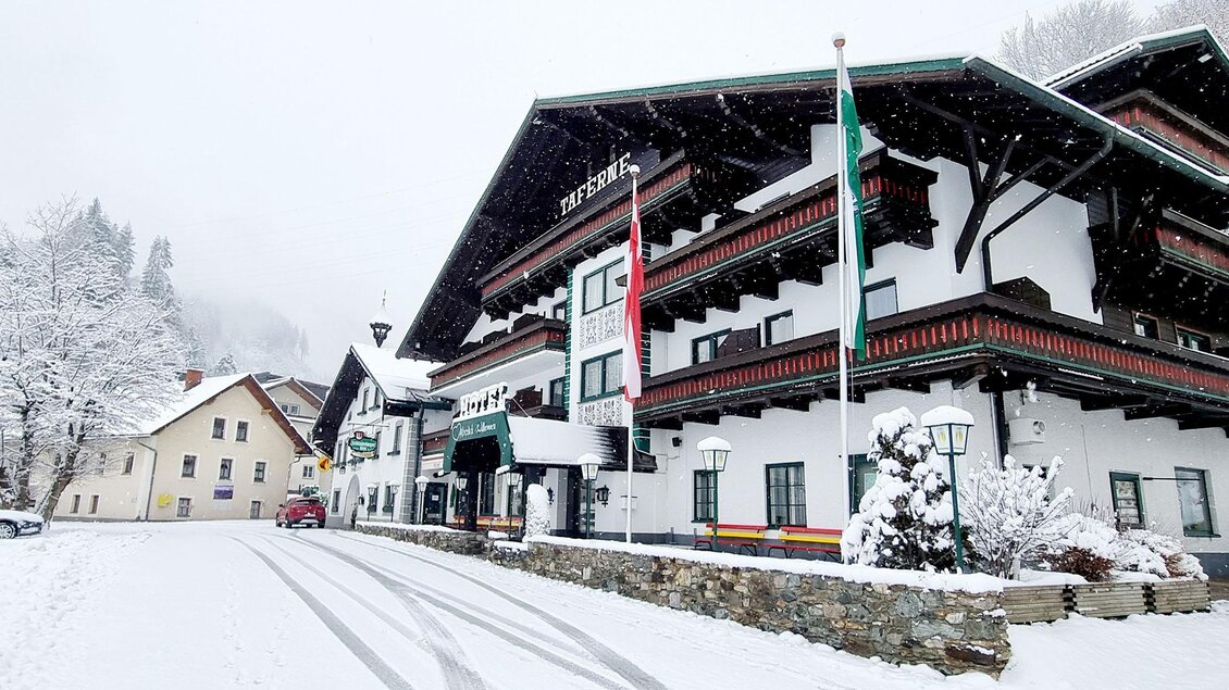 Ein schönes Hotel im Schnee mit traditioneller Architektur. Die Umgebung ist winterlich, mit einer ruhigen Straße und schneebedeckten Bäumen. | © Hotel Taferne