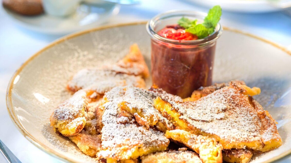 Ein Teller mit frittierten Teigstücken, bestreut mit Puderzucker. Dazu gibt es ein Glas mit Erdbeermarmelade. | © Hotel Seevilla Altaussee
