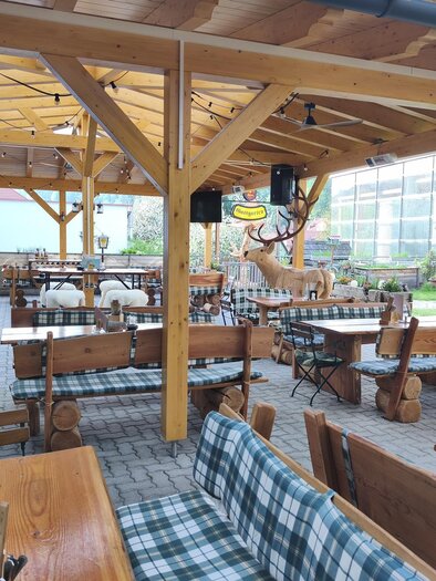 A cozy restaurant with a wooden veranda and outdoor tables. The decor has a rustic design with checkered tablecloths. | © Brauhaus Murau
