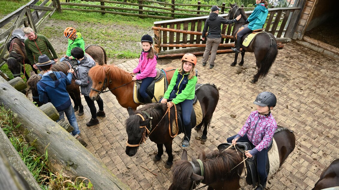 Eine Gruppe von Kindern und Erwachsenen bereitet sich auf einen Ausritt auf Ponys vor. Die Umgebung ist grün und natürlich, mit einem Holzzaun im Hintergrund. | © Breilerhof