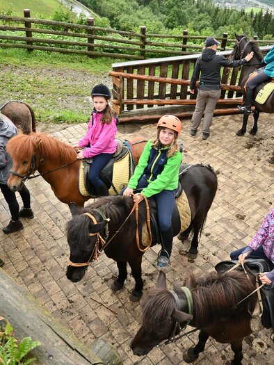 Eine Gruppe von Kindern und Erwachsenen bereitet sich auf einen Ausritt auf Ponys vor. Die Umgebung ist grün und natürlich, mit einem Holzzaun im Hintergrund. | © Breilerhof