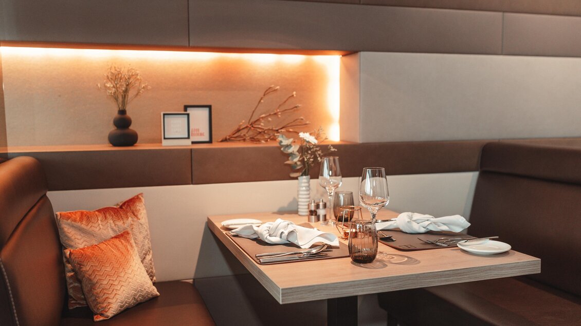 Ein eleganter Tisch in einem modernen Restaurant mit gemütlichen Sitzen. Sanfte Beleuchtung und dekorative Elemente schaffen eine einladende Atmosphäre. | © Thermenhotel Kowald