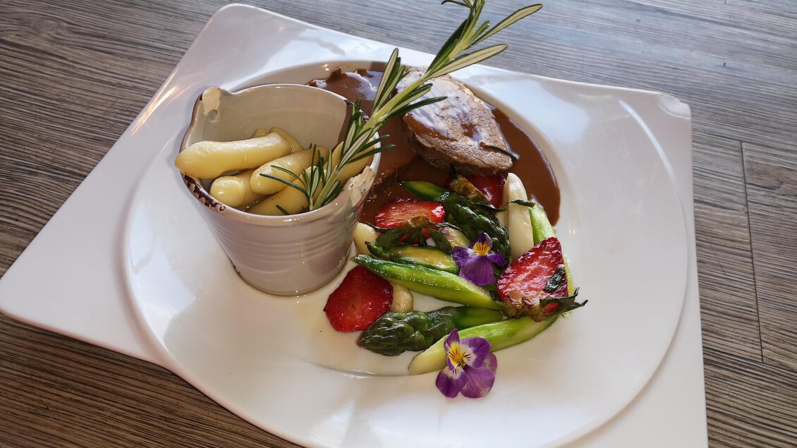 Ein schön angerichteter Teller mit gegrilltem Fleisch, Spargel und frischen Erdbeeren. Dazu gibt es eine kleine Schale mit Sauce und frischen Kräutern. | © Hotel Restaurant Perschler