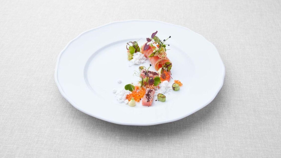 Ein kunstvoll arrangiertes Gericht auf einem weißen Teller. Es besteht aus verschiedenen frischen Zutaten, darunter Fisch und Gemüse. | © Tauroa GmbH