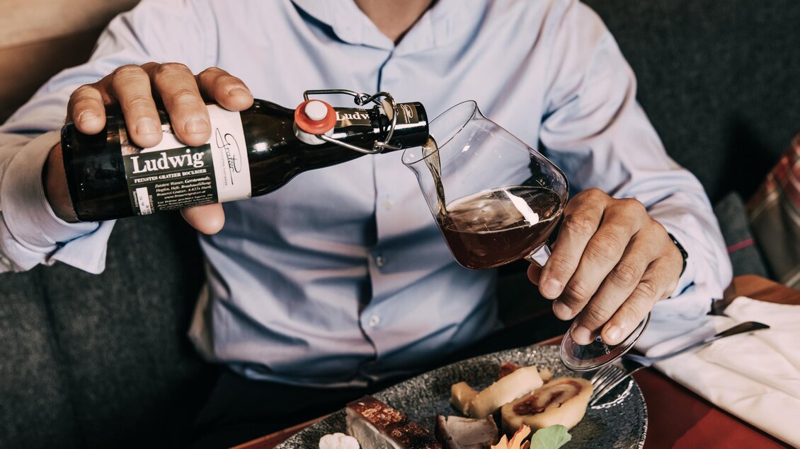 Eine Person schenkt ein Bier aus einer Flasche in ein Glas. Auf dem Tisch liegt ein ansprechendes Essen. | © Hotel Schwaigerhof