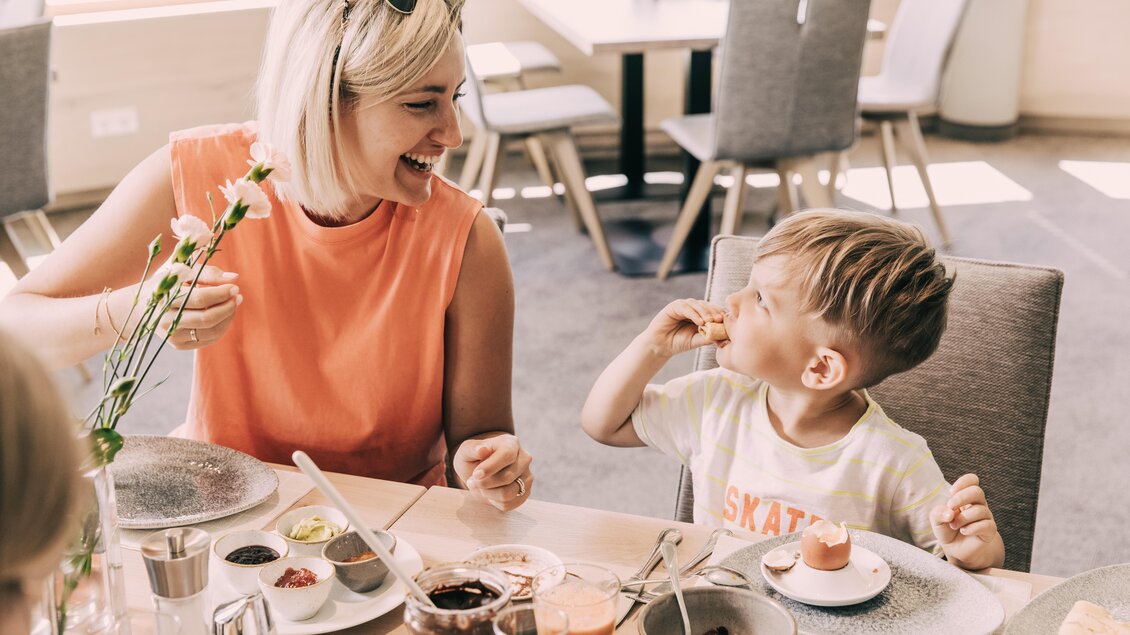 Eine fröhliche Mutter und ihr Sohn genießen gemeinsam das Frühstück. Der Tisch ist mit verschiedenen Speisen und Getränken gedeckt. | © Hotel Schwaigerhof