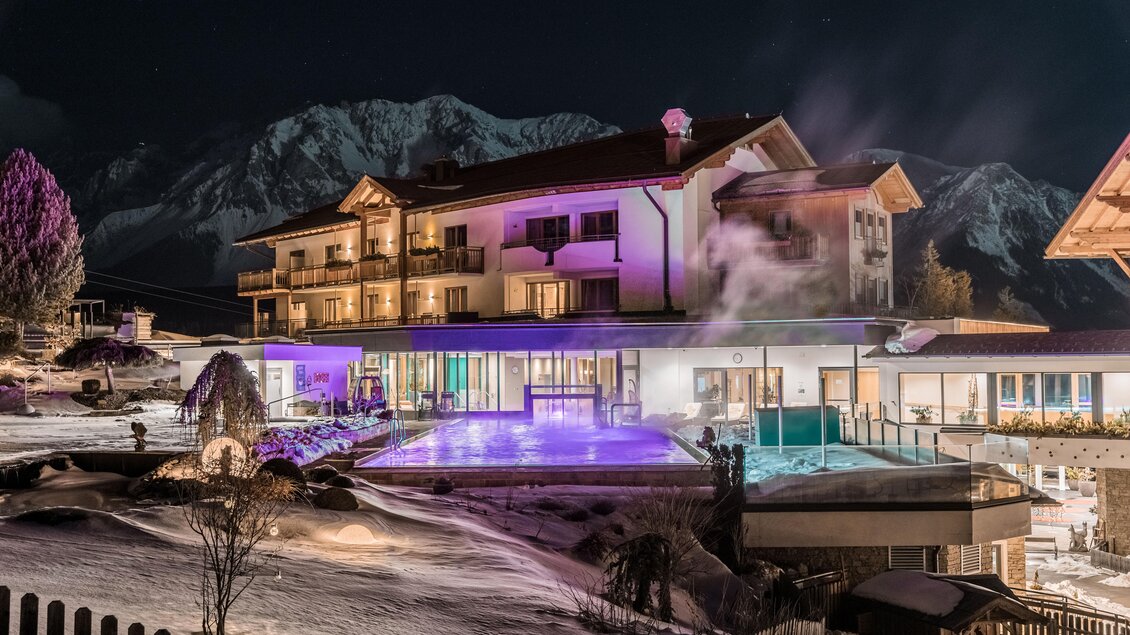 Ein Hotel mit einem beleuchteten Außenpool in einer schneebedeckten Landschaft bei Nacht. Im Hintergrund sind Berggipfel sichtbar. | © Hotel Schwaigerhof