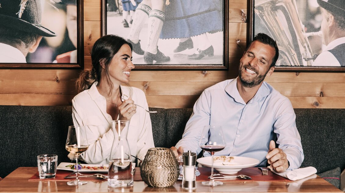 Ein Paar sitzt an einem Tisch in einem gemütlichen Restaurant. Sie lachen und genießen ein schönes Essen in entspannter Atmosphäre. | © Hotel Schwaigerhof