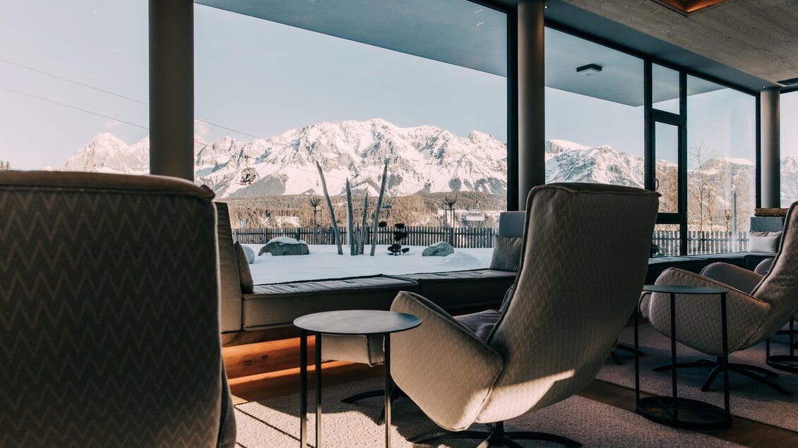 Eine gemütliche Lounge mit modernen Sesseln und einem Blick auf schneebedeckte Berge. Das große Fenster lässt viel Tageslicht herein und bietet eine entspannende Aussicht. | © Hotel Schwaigerhof