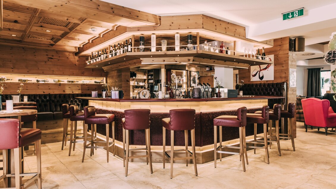 Eine elegante Bar mit Holzverkleidung und stilvollen roten Stühlen. Der Bartresen ist gut gefüllt und schafft eine einladende Atmosphäre. | © Hotel Schwaigerhof