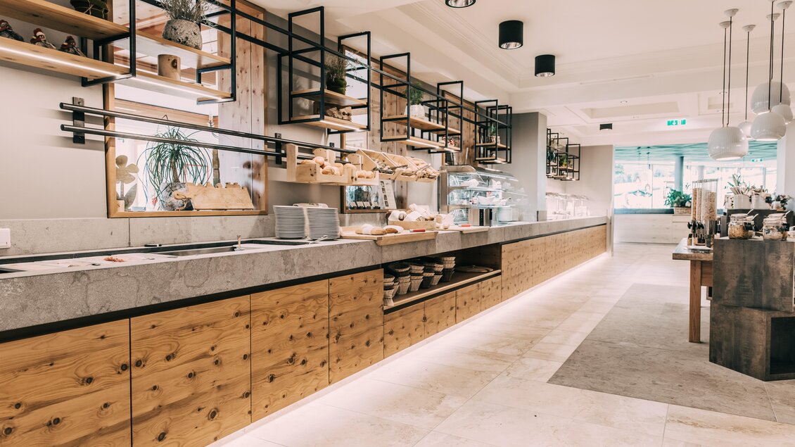 Ein modernes Café mit einer Holz-Theke und eleganten Regalen. Es ist hell und freundlich, mit vielen Pflanzen und einem einladenden Ambiente. | © Hotel Schwaigerhof