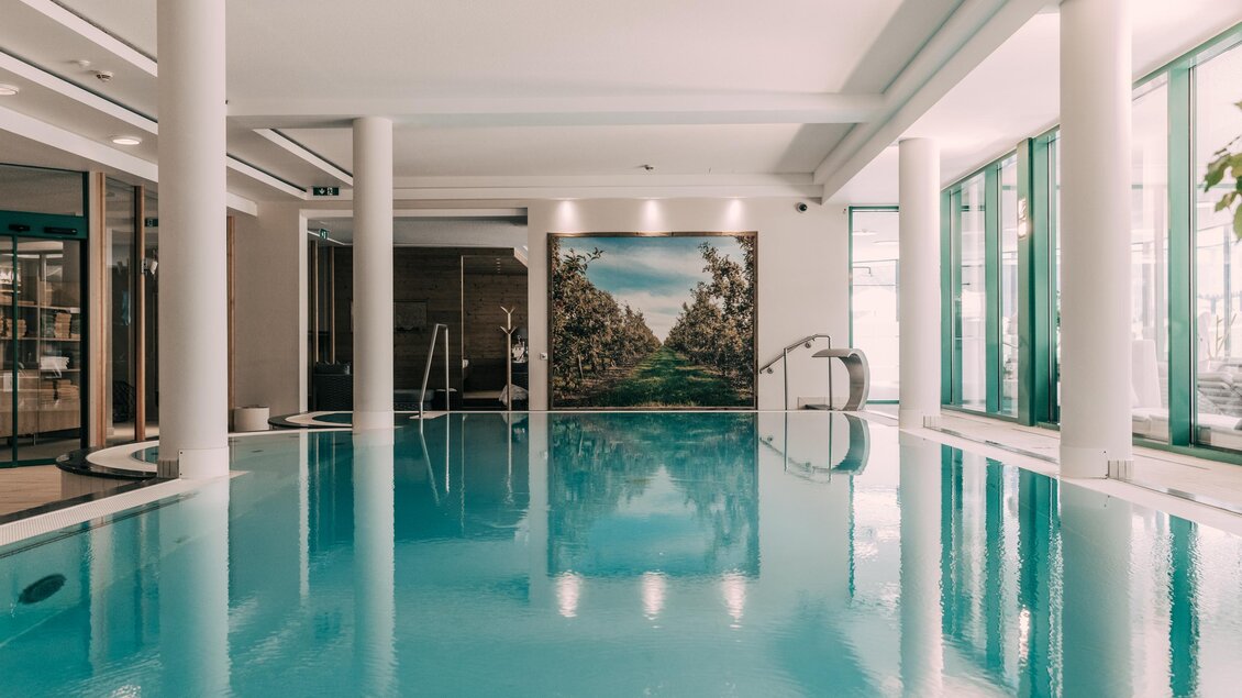 Ein elegantes Hallenbad mit klarem Wasser und großen Fenstern. Die Wände sind mit einem schönen Landschaftsbild dekoriert. | © Hotel Schwaigerhof