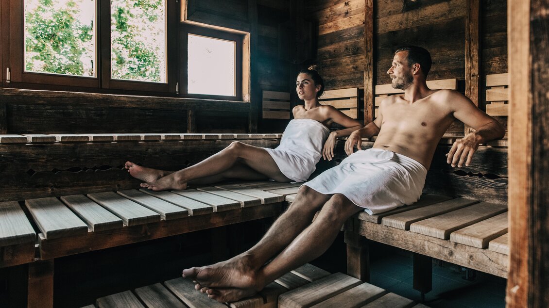 Ein Paar entspannt in einer Holzsauna. Sie sitzen auf Bänken und genießen die angenehme Atmosphäre. | © Hotel Schwaigerhof