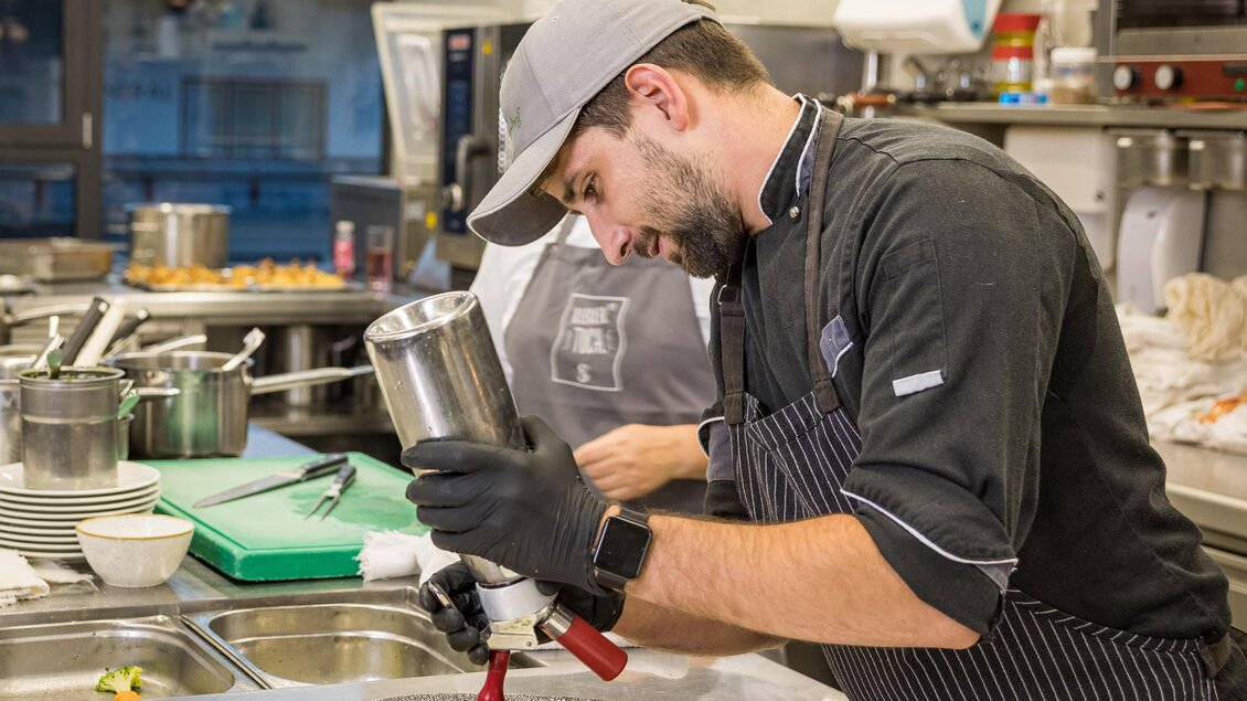 Ein Koch bereitet ein Gericht in einer modernen Küche vor. Er verwendet eine Spritzflasche, um die Speisen kunstvoll anzurichten. | © Netzwerk Kulinarik wildbild