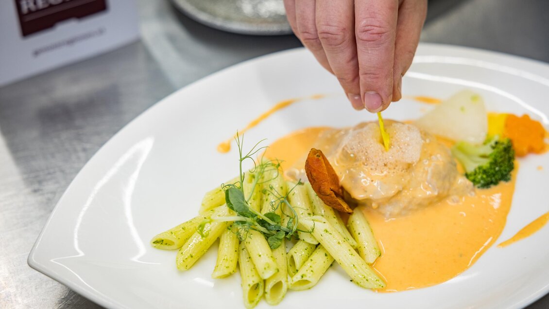 Ein Teller mit Pasta und Gemüse, während jemand eine Zutat auf das Hauptgericht gibt. Die Präsentation ist ansprechend und zeigt eine feine Küche. | © Netzwerk Kulinarik wildbild