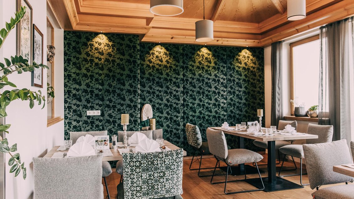 Ein elegant eingerichtetes Restaurant mit einem dekorativen grünen Wanddesign. Tische sind mit weißen Tischdecken und Geschirr eingedeckt, und die Beleuchtung schafft eine gemütliche Atmosphäre. | © Hotel Schwaigerhof