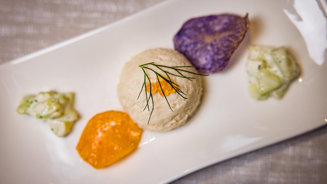 Ein kunstvoll angerichteter Teller mit einer kleinen Portion Creme, begleitet von bunten Saucen und frischen Kräutern. Die Farben und Anordnung machen das Gericht ansprechend und appetitlich. | © Netzwerk Kulinarik wildbild