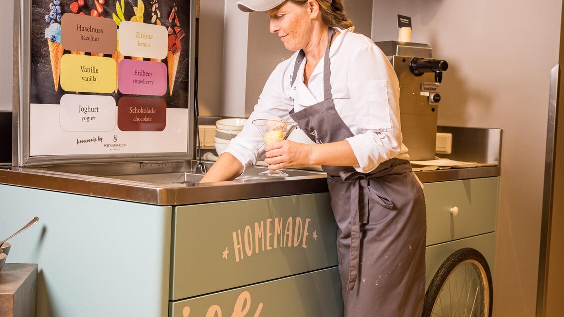 Eine Frau bereitet Speiseeis an einem hübschen Eisstand. Der Stand ist in sanften Farben gestaltet und hat ein gestreiftes Dach. | © Netzwerk Kulinarik wildbild