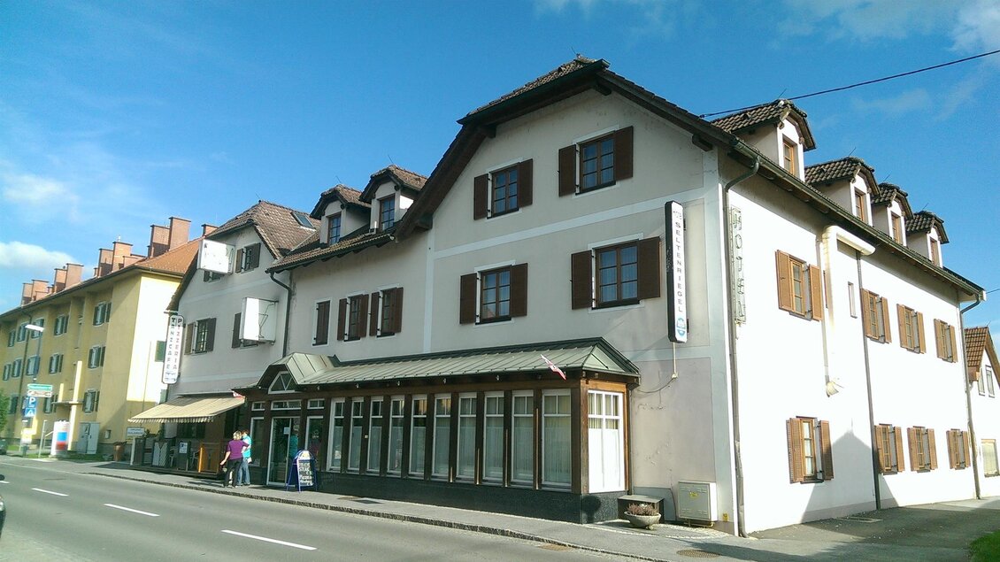 Ein großes, mehrstöckiges Gebäude mit braunen Fensterläden und einem schönen Dach. Neben der Straße stehen einige Personen und ein weiteres Gebäude ist sichtbar. | © Hotel Seltenriegel