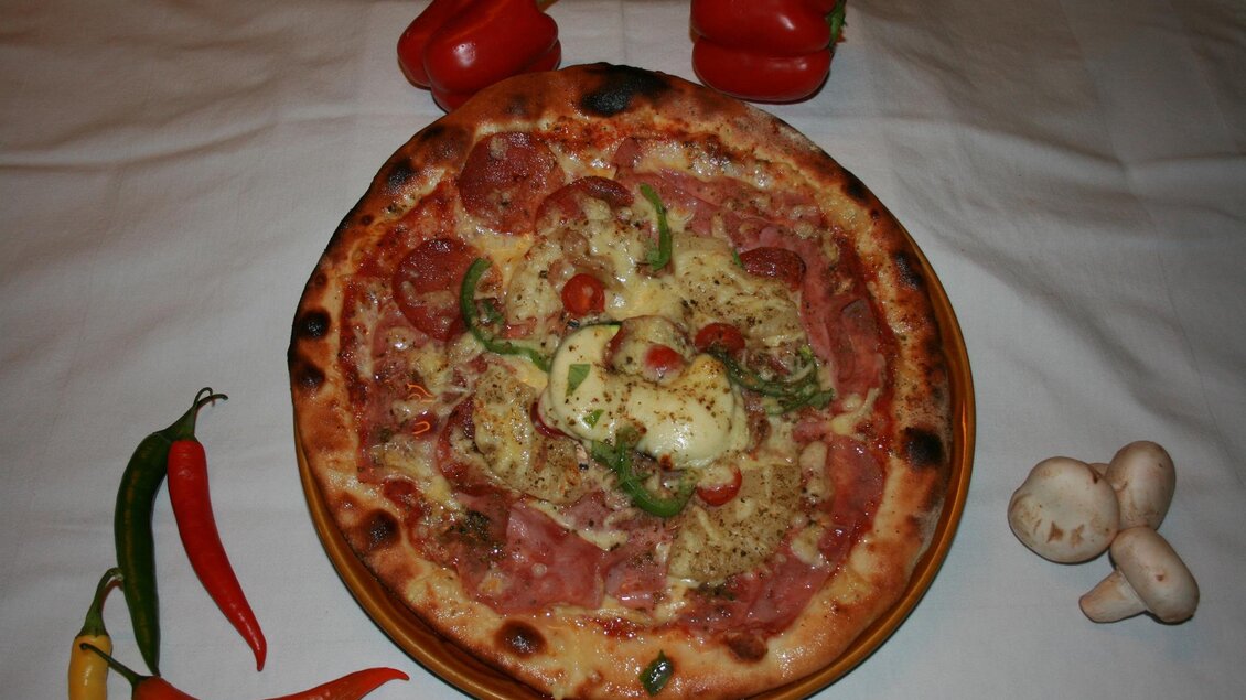 Eine frisch gebackene Pizza mit verschiedenen Zutaten wie Salami, Paprika und Pilzen. Daneben liegen einige frische Chili und Paprika. | © Hotel Seltenriegel