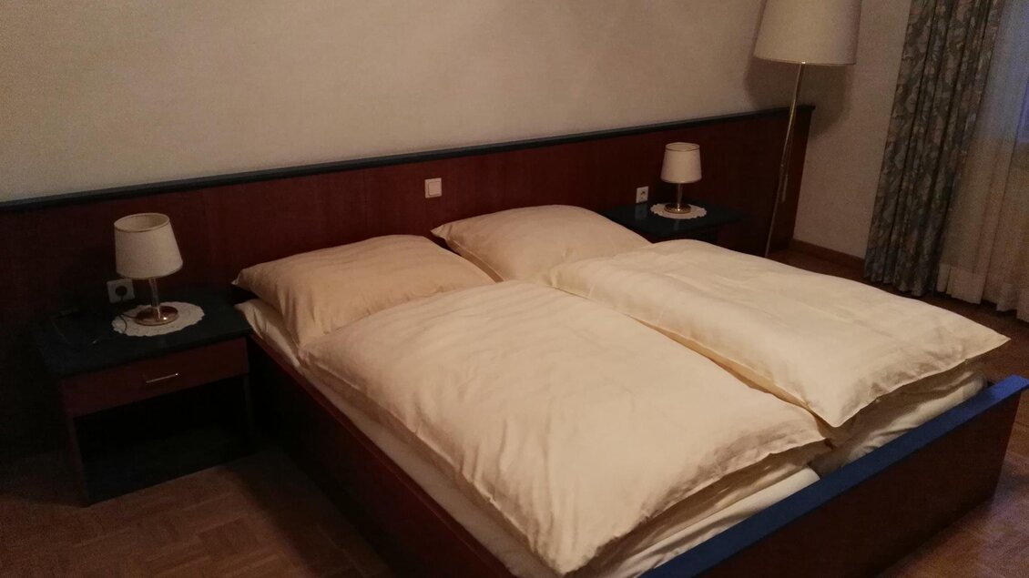 Ein gemütliches Schlafzimmer mit einem Doppelbett und zwei Nachttischen. Die Beleuchtung wird durch eine Stehlampe und zwei Tischlampen unterstützt. | © Hotel Seltenriegel
