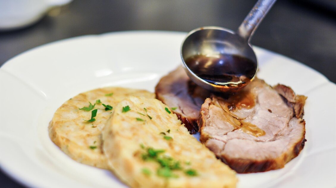 Ein Teller mit zartem Fleisch und zwei Scheiben Knödel. Darauf wird eine dunkle Sauce gegossen. | © Teuschler Mogg