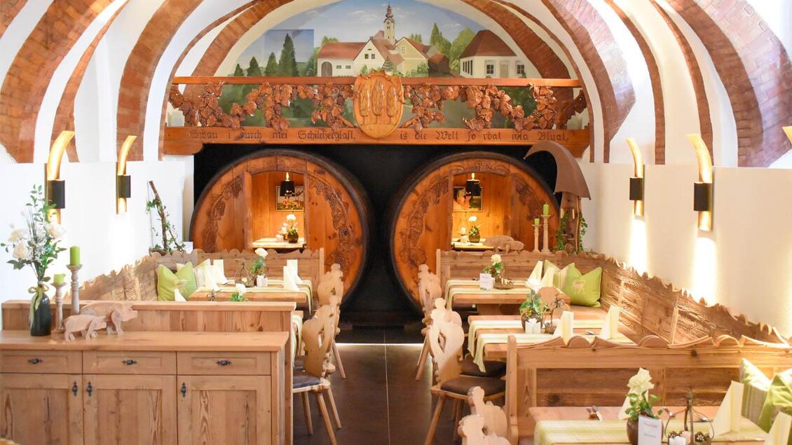 Ein gemütliches Restaurant mit Holzstühlen und Tischen. An den Wänden sind kunstvolle Malereien und große Weinfässer zu sehen. | © Desiree Zwanzleitner