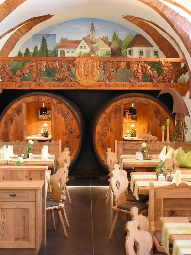 Ein gemütliches Restaurant mit Holzstühlen und Tischen. An den Wänden sind kunstvolle Malereien und große Weinfässer zu sehen. | © Desiree Zwanzleitner