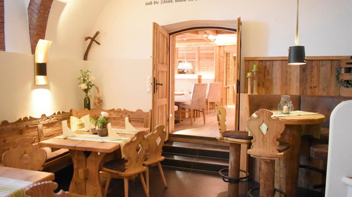 Ein gemütliches Restaurant mit rustikalem Holzmobiliar und gut gedeckten Tischen. Im Hintergrund sieht man einen weiteren Essbereich mit warmem Licht und einladender Atmosphäre. | © Desiree Zwanzleitner