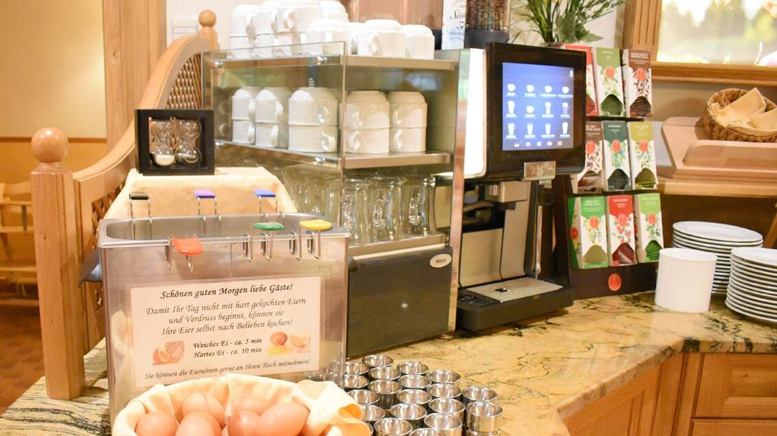 Ein Frühstücksbuffet mit einer Kaffeemaschine, Gläsern und Tellern. Auf dem Tisch sind frische Eier und verschiedene Getränke vorhanden. | © Desiree Zwanzleitner
