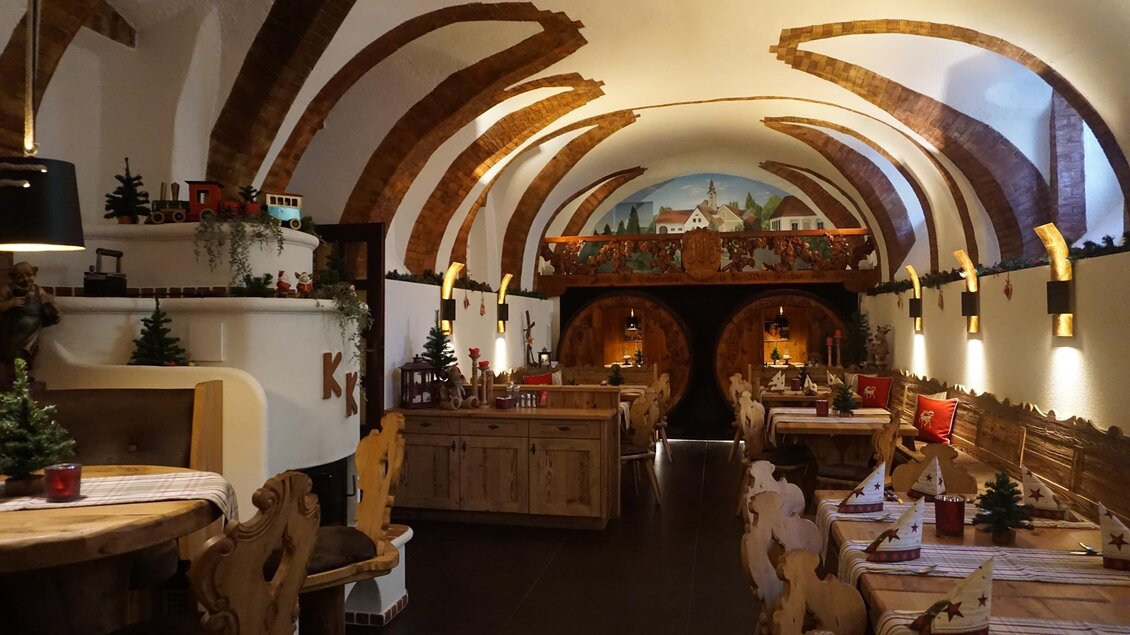 Ein gemütliches Restaurant mit Holzdekor und einem gewölbten Dach. An den Wänden sind malerische Szenen sowie kleine Weihnachtsdekorationen zu sehen. | © Kloepferkeller