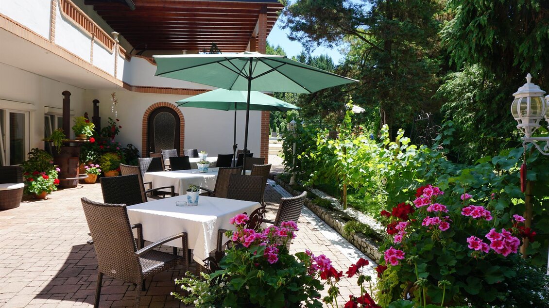 Ein einladender Außenbereich mit Tischen und Stühlen unter einem Sonnenschirm. Bunte Blumen und grüne Pflanzen umgeben den gemütlichen Platz. | © Kloepferkeller