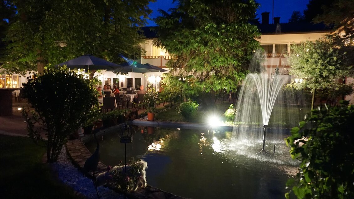 Ein schöner Garten in der Nacht mit einem beleuchteten Brunnen und gemütlichen Sitzbereichen. Die Atmosphäre ist einladend und entspannend. | © Kloepferkeller