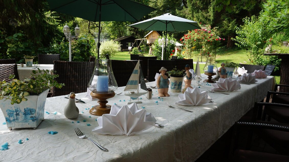 Ein schön gedeckter Tisch im Freien mit Sonnenschirmen und dekorativen Elementen. Umgeben von grüner Natur und blühenden Pflanzen. | © Kloepferkeller