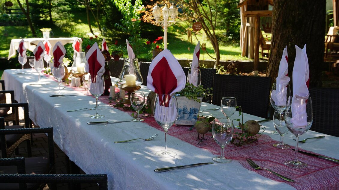 Ein schön gedeckter Tisch im Freien mit roten und weißen Servietten. Die Umgebung ist grün und einladend, ideal für eine Feier. | © Kloepferkeller