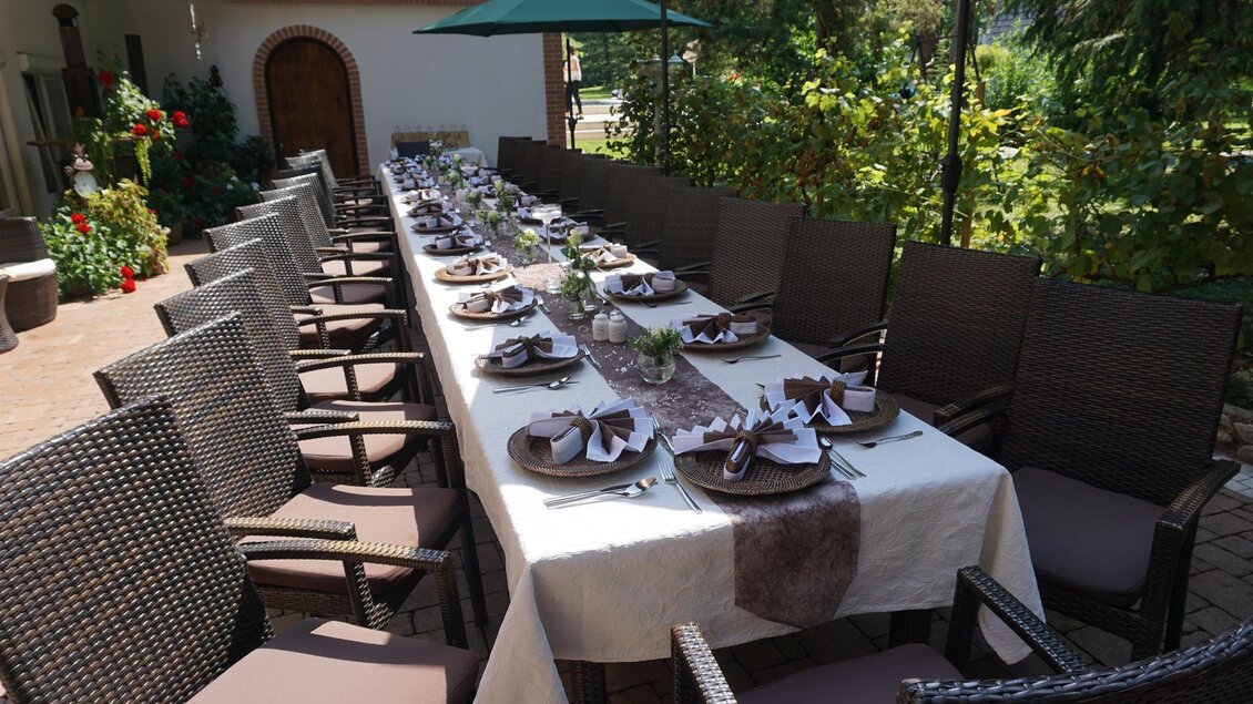 Ein schön gedeckter Tisch im Freien mit Stühlen und Sonnenschirmen. Der Tisch ist für eine festliche Mahlzeit vorbereitet, umgeben von Pflanzen. | © Kloepferkeller