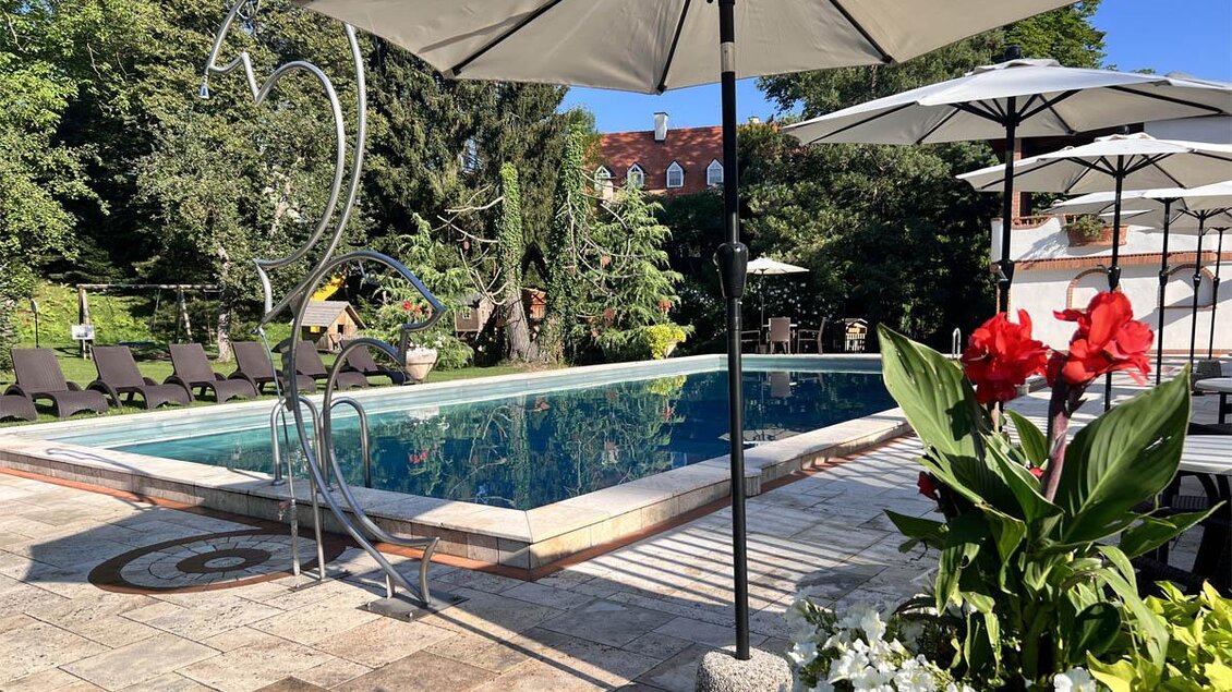 Ein schöner Pool umgeben von Liegen und Sonnenschirmen in einer grünen Oase. Bunte Blumen bringen Farbe in die entspannende Atmosphäre. | © Desiree Zwanzleitner